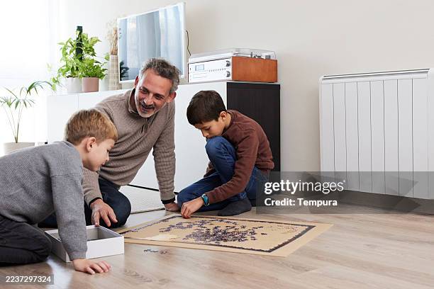 ein vater und ihre kinder vergnügen sich gemeinsam zu hause mit einem lustigen puzzle. - heizung stock-fotos und bilder