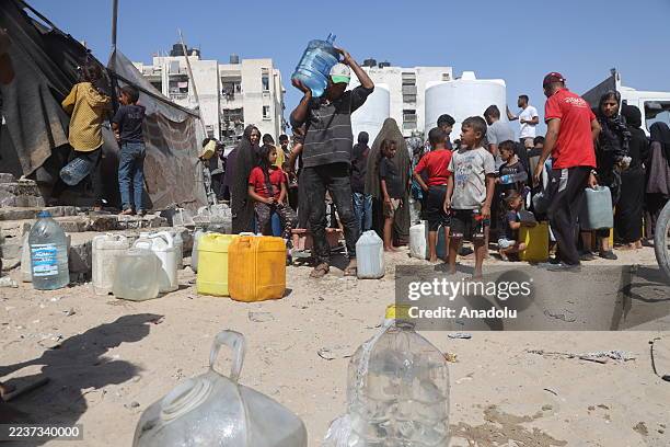 Palestinians, including children, who get water from tankers, carry water in canisters as Palestinians, who migrated to southern regions due to the...
