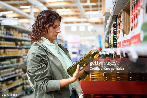 woman shopping comparing olive oil prices in supermarket - inflação imagens e fotografias de stock