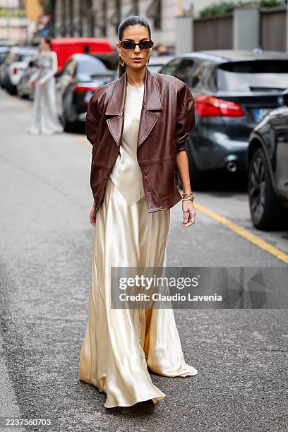 Guest is seen wearing an oversized brown leather jacket with structured shoulder pads over a long champagne-colored silk dress, black sunglasses and...