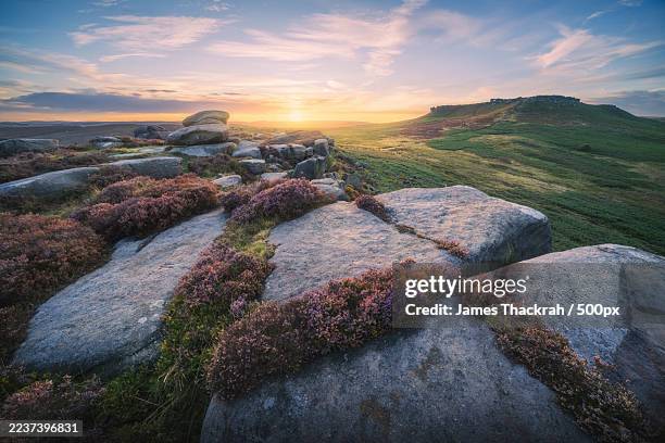 dramatic sunset over a rugged, heather-covered landscape with large rock formations and rolling hills under a vast sky,hathersage,united kingdom,uk - peak district national park stock pictures, royalty-free photos & images