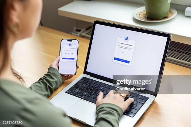 mujer escribiendo código 2fa desde un teléfono inteligente en una computadora portátil en un espacio de trabajo contemporáneo - contraseña fotografías e imágenes de stock