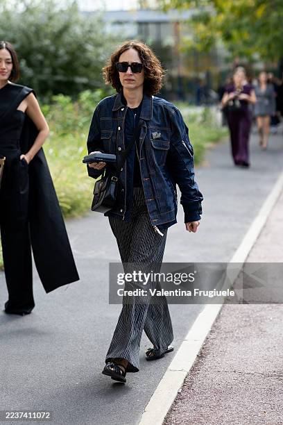 Guest wears brown sunglasses, black and white striped trousers, a denim cargo jacket, black leather shoes, a black sweater and a black leather...