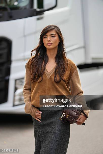 Clara Kong Villa wears long dark brown hair with loose waves and a side part, a dark brown leather shoulder bag with gold-toned hardware carried...