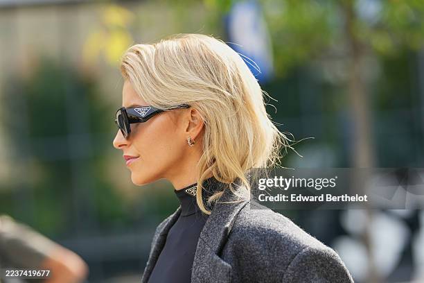 Caroline Daur wears blonde shoulder-length hair parted slightly off-center with soft waves, small gold hoop earrings, black sunglasses, a charcoal...