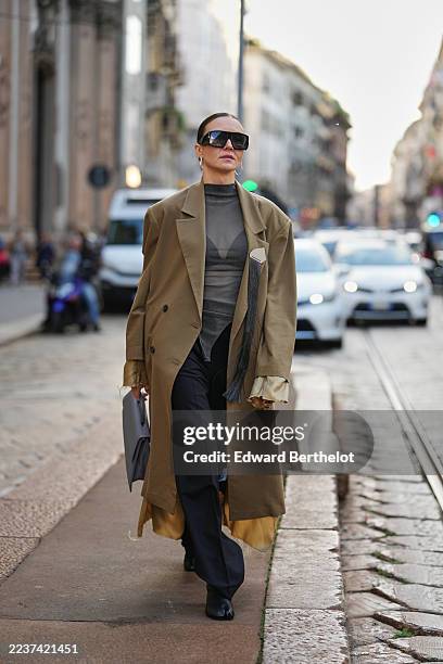 Guest wears a sleek center-parted low bun dark brown hairstyle, oversized rectangular black sunglasses, silver hoop earrings, a grey purple...