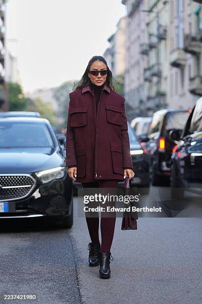 Tamara Kalinic wears long dark brown hair pulled back from the face in a half-up center-part style, brown rectangular sunglasses, a handheld burgundy...