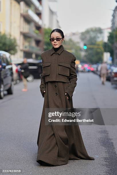 Jenny Tsang wears hair pulled back into a low bun, medium-length dark brown hair with a center part, small rectangular sunglasses with dark lenses...