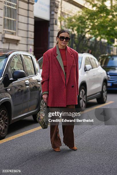 Guest wears a slicked-back low bun hairstyle, oversized dark brown sunglasses, gold hoop earrings and gold rings and a gold bracelet, a green and...