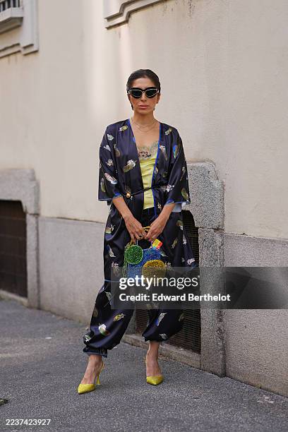 Guest wears dark brown hair pulled back into a low slicked-back bun, black cat-eye sunglasses with gold trim, small gold hoop earrings and layered...