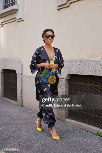 Guest wears dark brown hair pulled back into a low slicked-back bun, black cat-eye sunglasses with gold trim, small gold hoop earrings and layered...