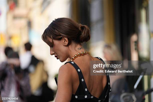 Ludovica Ragazzo wears a loose low bun hairstyle with center-parted curtain bangs, a chunky gold metal beaded necklace, a black sleeveless dress with...