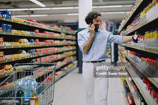 man grocery shopping in supermarket, pushing cart and selecting products - tin man stock pictures, royalty-free photos & images