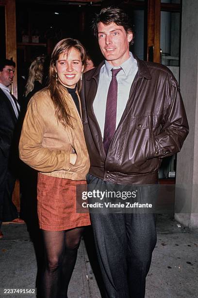 American actress and singer Dana Morosini, wearing a beige jacket and a burnt orange miniskirt, and her partner, American actor Christopher Reeve,...