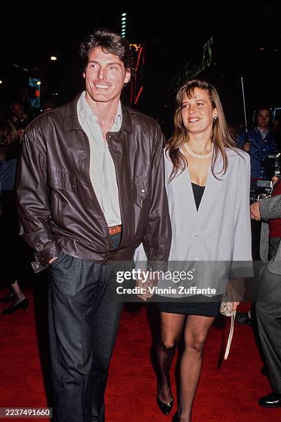 American actor Christopher Reeve, wearing a brown leather jacket over a white shirt with dark grey trousers, and his partner, American actress and...