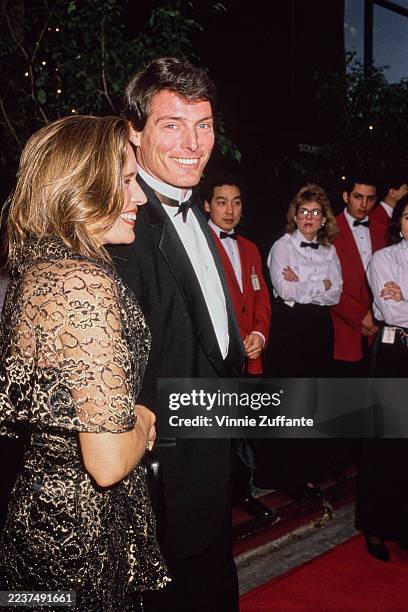 American actress and singer Dana Morosini, wearing a sheer gold evening wrap over a black dress, and her partner, American actor Christopher Reeve,...