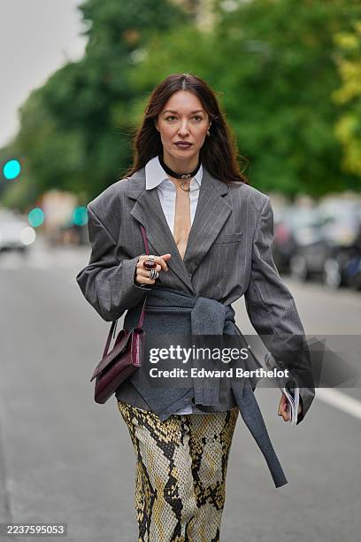Guest wears long brown hair in loose waves with a center part, a black leather choker necklace with a silver O-ring and small silver hoop earrings...