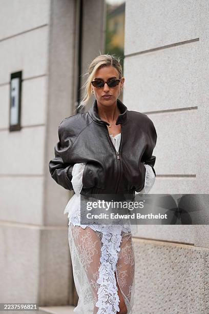 Emili Sindlev wears pulled-back blonde hair in a low bun with a slight side part, rectangular tortoiseshell sunglasses, gold hoop earrings and a thin...