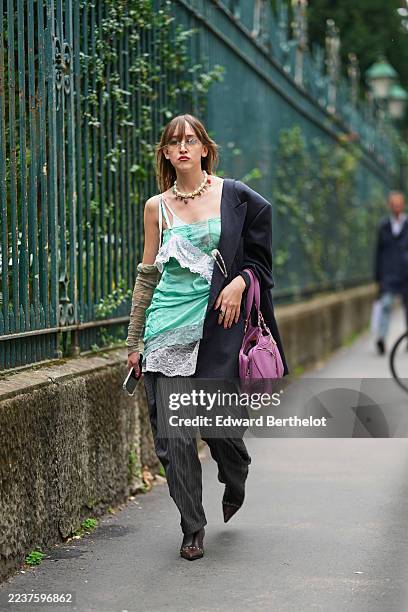 Guest wears shoulder-length light brown hair with straight bangs and a slight center part, clear rimmed eyeglasses, a beaded multicolored necklace...