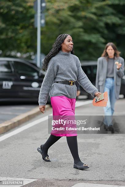 Guest wears long black braided hair with a center part, a grey fuzzy knit turtleneck sweater, a black leather belt from Tod's with a gold T-shaped...