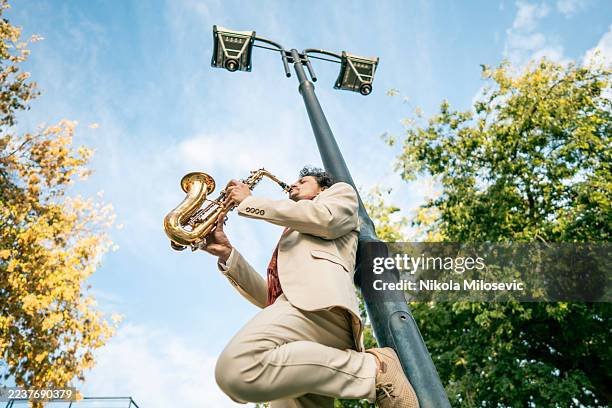 energetic street saxophonist in a light beige suit playing outdoors under a street lamp - bandstand stock pictures, royalty-free photos & images