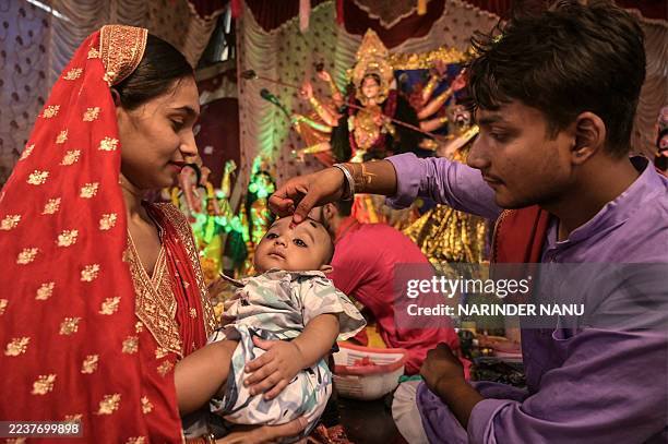 Priest puts 'tilak', or holy mark, on the forehead of a child in front of an idol of the Hindu goddess Durga during the Durga Puja festival in...