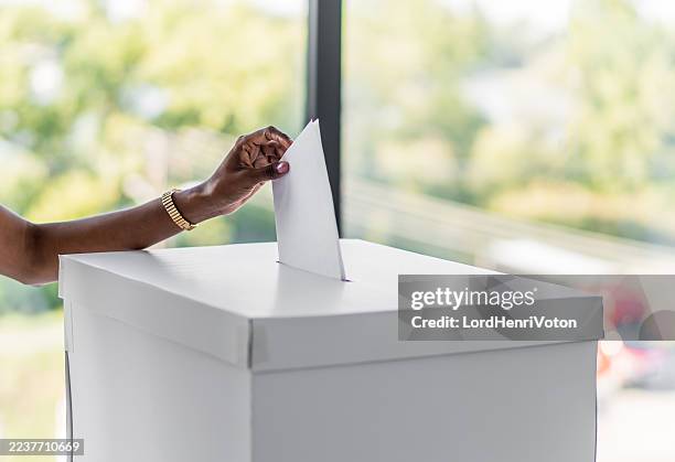black hand casting ballot in vote box on election day - stembiljet stockfoto's en -beelden