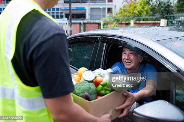 male volunteer hands out food to a senior adult driver at drive through food bank - banco alimentar imagens e fotografias de stock