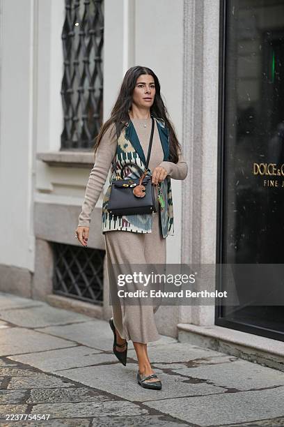Guest wears long dark brown hair worn loose with a center part, a silver necklace with a small round pendant, a black leather top-handle satchel...