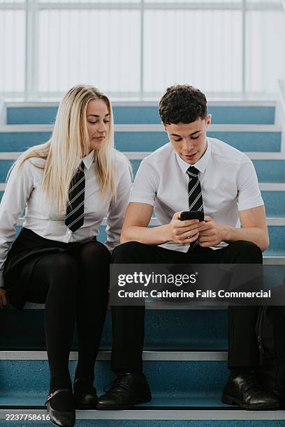 students in school uniform sitting on stairs using mobile phones during break time - social media ban stock pictures, royalty-free photos & images