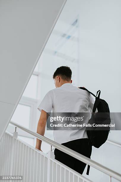 senior schoolboy walking upstairs in a modern building with a backpack during the school day. - schoolboy stock pictures, royalty-free photos & images