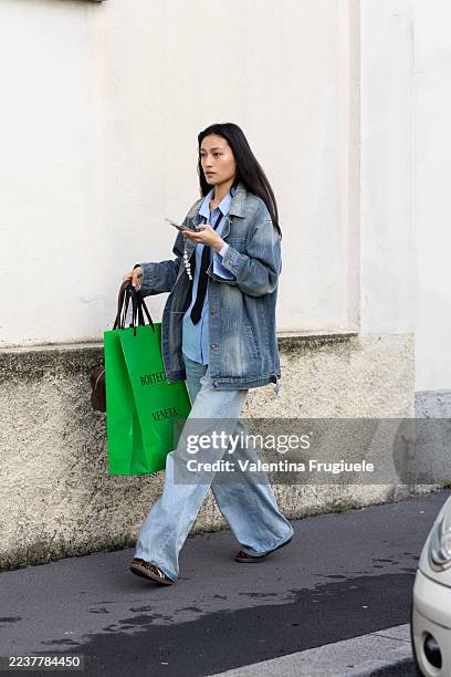 Model wears a green maxi Bottega Veneta bag, a denim jacket, blue jeans, a light blue shirt and brown sneakers outside Bottega Veneta show during the...