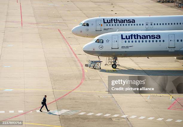 Dpatop - 30 September 2025, Hesse, Frankfurt/Main: A man walks past two Lufthansa aircraft parked in an open area in front of a maintenance hangar....