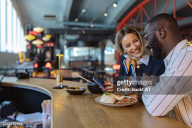 two coworkers enjoy a business lunch at a stylish food market restaurant and using smartphone - lunchpauze stockfoto's en -beelden