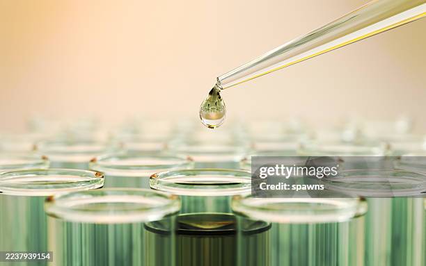 testflüssigkeit aus grünem glas pipettiert in reagenzgläser auf gelbem reflektierendem hintergrund - chemiker stock-fotos und bilder