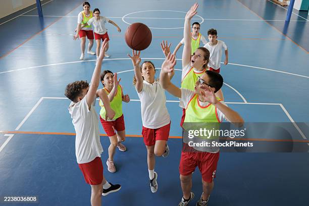 group of diverse kids playing basketball in school gym. - high school basketball stock pictures, royalty-free photos & images