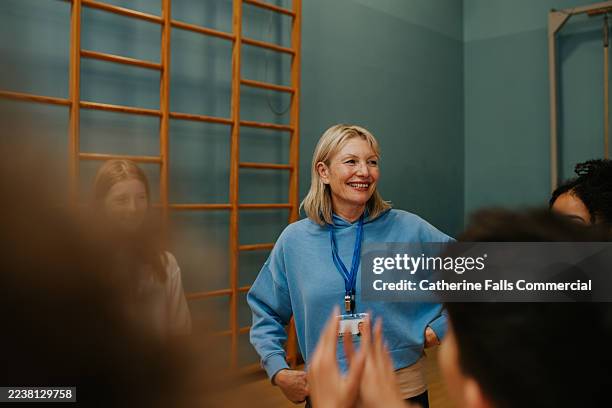 group of students engaged in conversation with a teacher in a school gym during a physical education class - ausbilder stock-fotos und bilder