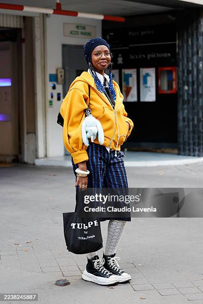 Guest wears a navy blue knit beanie, an oversized yellow hooded jacket, a white shirt underneath, a dark blue patterned culottes, white lace...