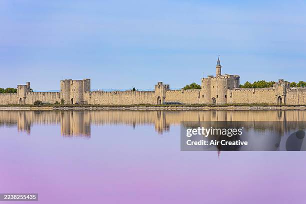 photograph of the medieval part of the town of aigues-mortes and its reflection in a pink salt marsh, gard, france - salt marsh stock pictures, royalty-free photos & images