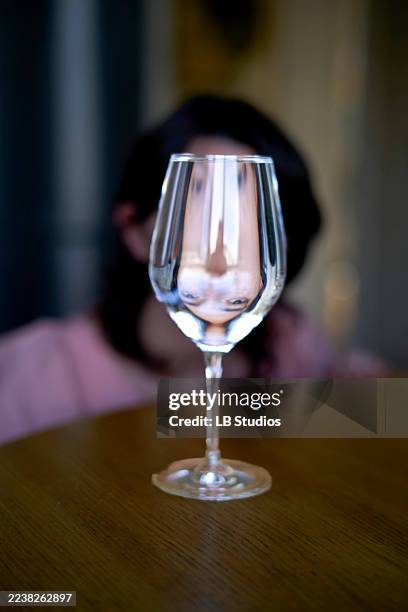 glass of water with a distorted face reflection on a wooden table - refraction people photos et images de collection