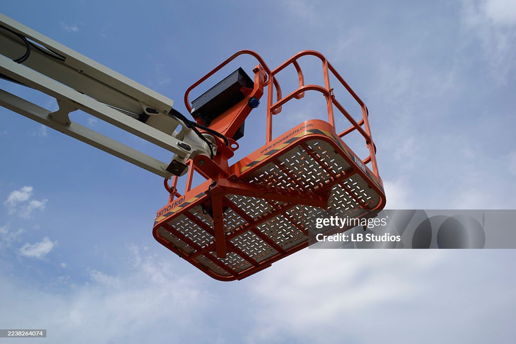 Orange cherry picker basket elevated against a clear blue sky with a few clouds. Germany