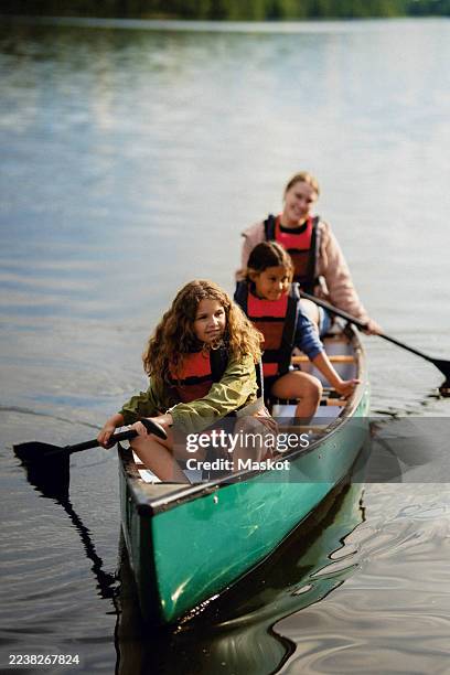 smiling multiracial girls sitting with female instructor in canoe on lake at summer camp - summer camp canoe stock pictures, royalty-free photos & images