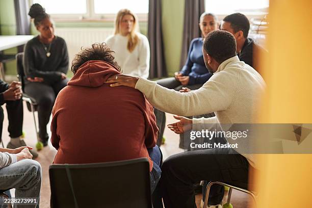 male counselor consoling sad teenage boy during group therapy session in school - group therapy stock pictures, royalty-free photos & images