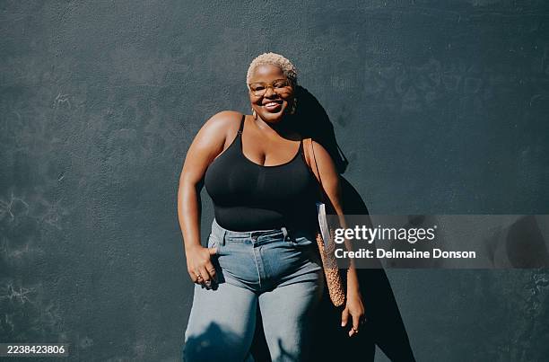 selbstbewusste junge schwarze frau, die im freien vor strukturierter wand lächelt sommer freizeitkleidung - halbnahe-einstellung stock-fotos und bilder
