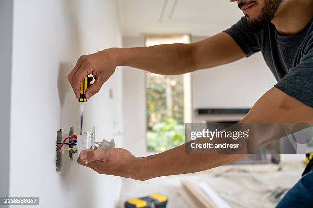 primer plano de un electricista instalando una toma de corriente en un sitio de construcción - toma eléctrica fotografías e imágenes de stock
