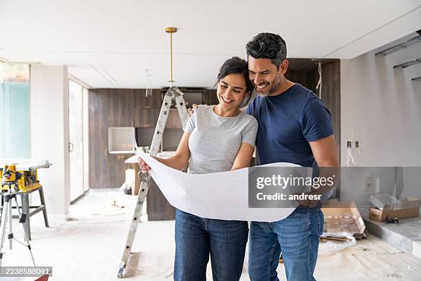 pareja feliz remodelando su casa y mirando un plano - renovación fotografías e imágenes de stock