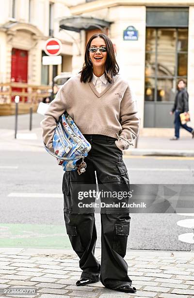 Guest is seen wearing a gray sweater, white shirt, black cargo pants, blue and white bag and silver sunglasses outside the Acne Studios show during...