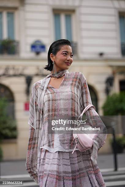 Stephanie Hui wears slicked-back short black hair, silver drop earrings, a pale pink leather top-handle bag, a sheer plaid chiffon blouse with a...