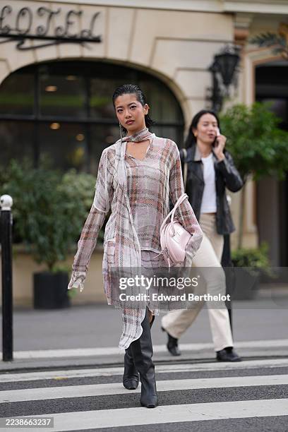 Stephanie Hui wears slicked-back short black hair, silver drop earrings, a pale pink leather top-handle bag, a sheer plaid chiffon blouse with a...