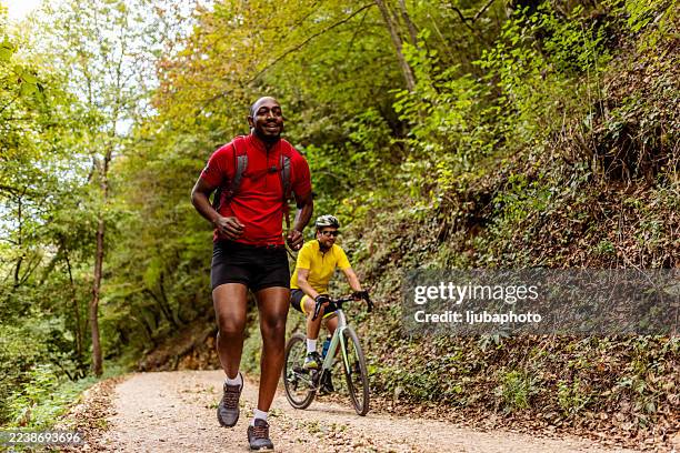 athletes running and biking on a forest trail in a bright outdoor fitness adventure - wielrennen stockfoto's en -beelden